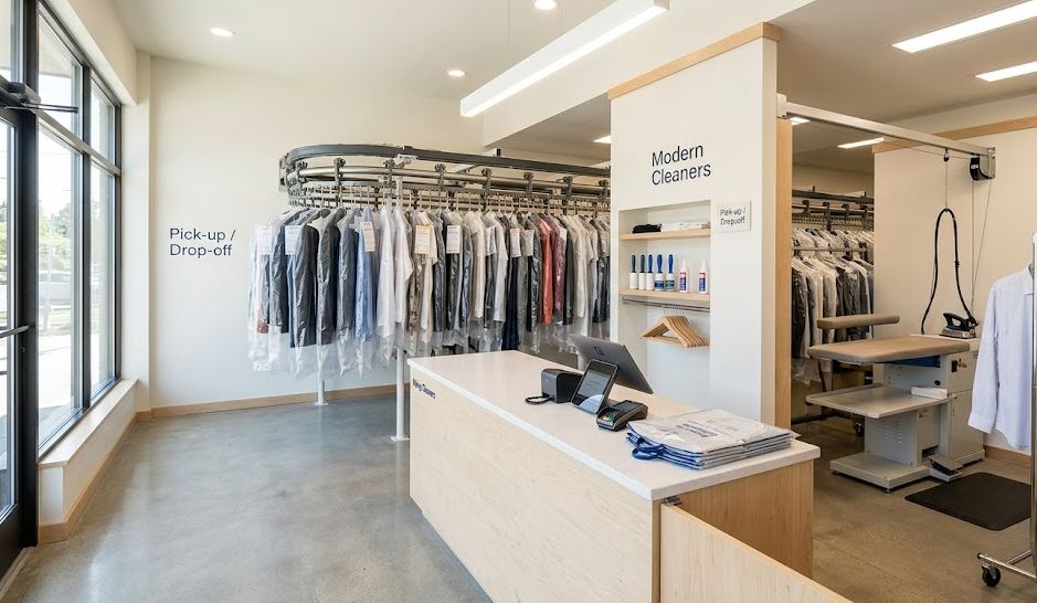 Interior of a modern dry cleaning business with garment conveyor and pressing equipment, representing startup costs.